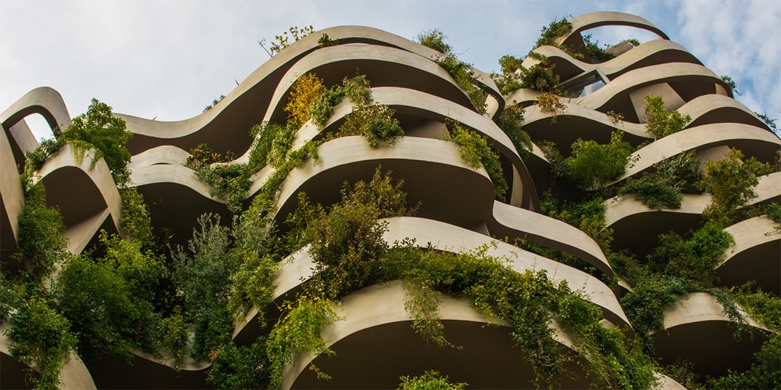 An organic-designed green building with curved balconies covered in lush plants, creating a vertical garden against the sky.