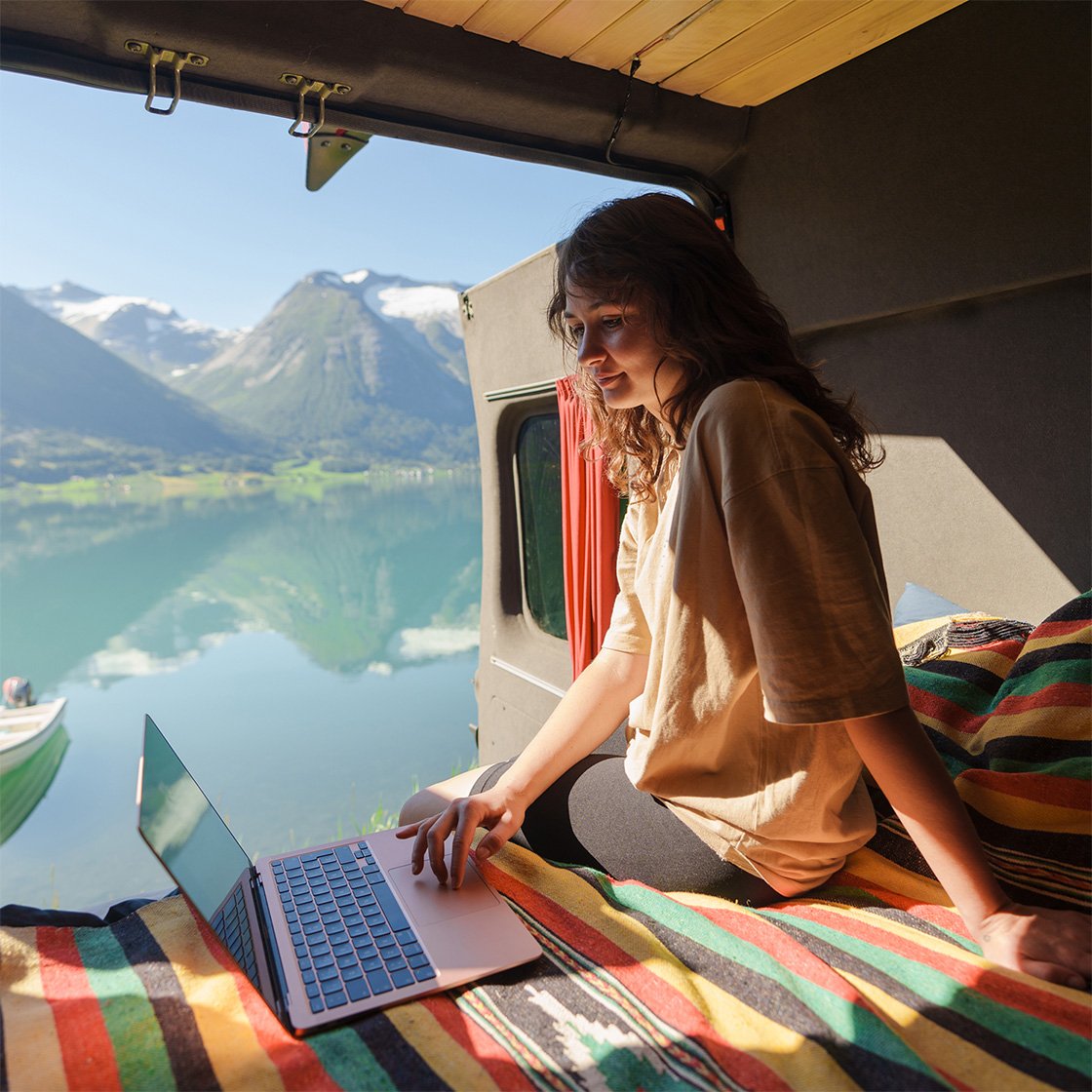 Young Caucasian woman sitting and working with laptop in camper van near the lake in Norway Young Caucasian woman sitting and working with laptop in camper van near the lake in Norway