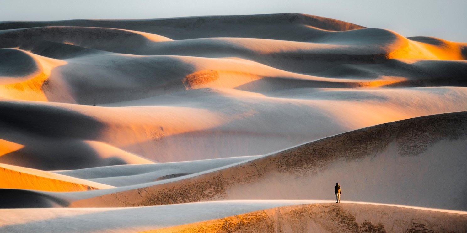 Tourist on top of massive sand dunes at sunset - stock photo