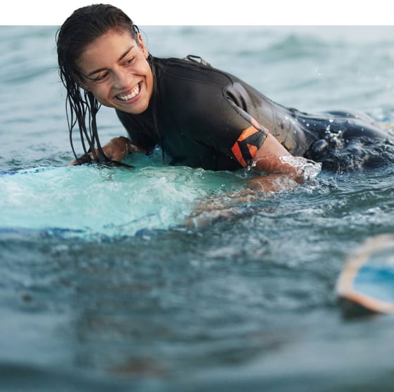 Woman on a surfboard smiling at her friend who is surfing too 