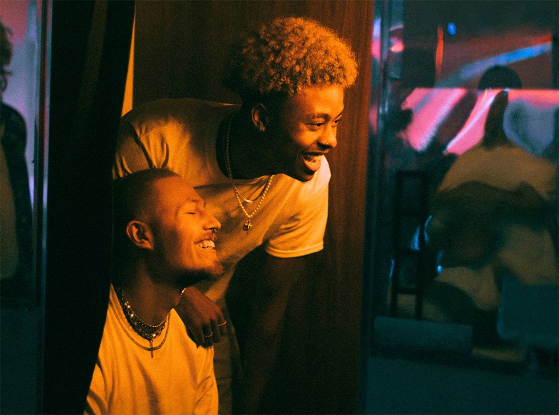 Two friends smiling and laughing together in warm indoor lighting with colourful reflections. Two friends smiling and laughing together in warm indoor lighting with colourful reflections.