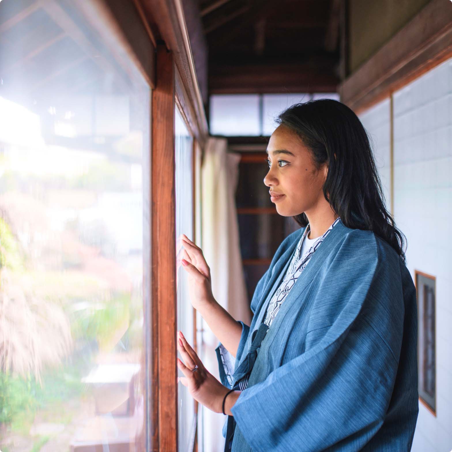 Woman looking out the window of a Japanese style home Woman looking out the window of a Japanese style home