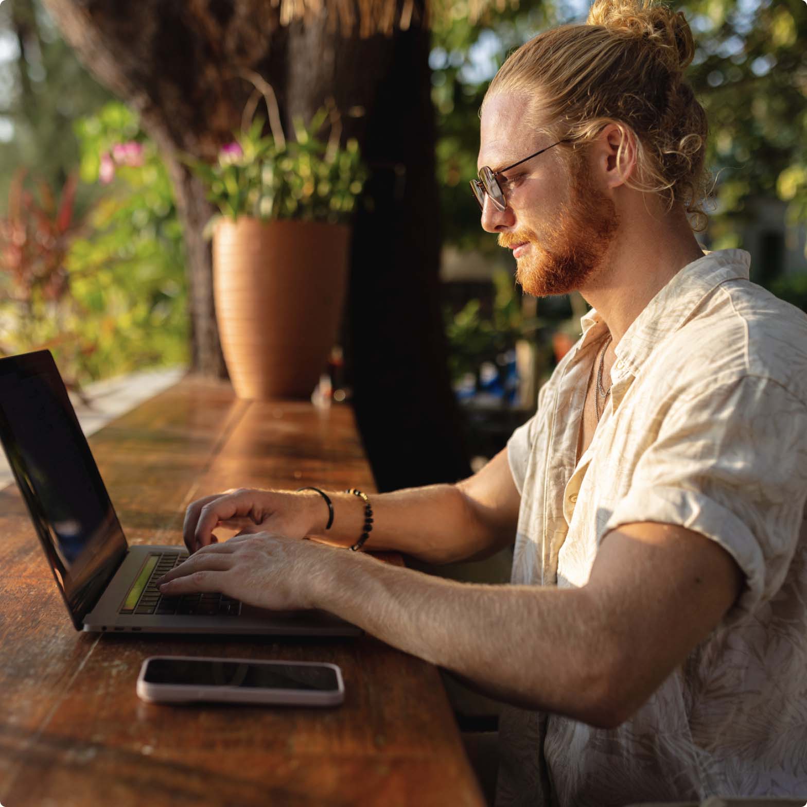 A man sitting at an outdoor cafe working on a laptop