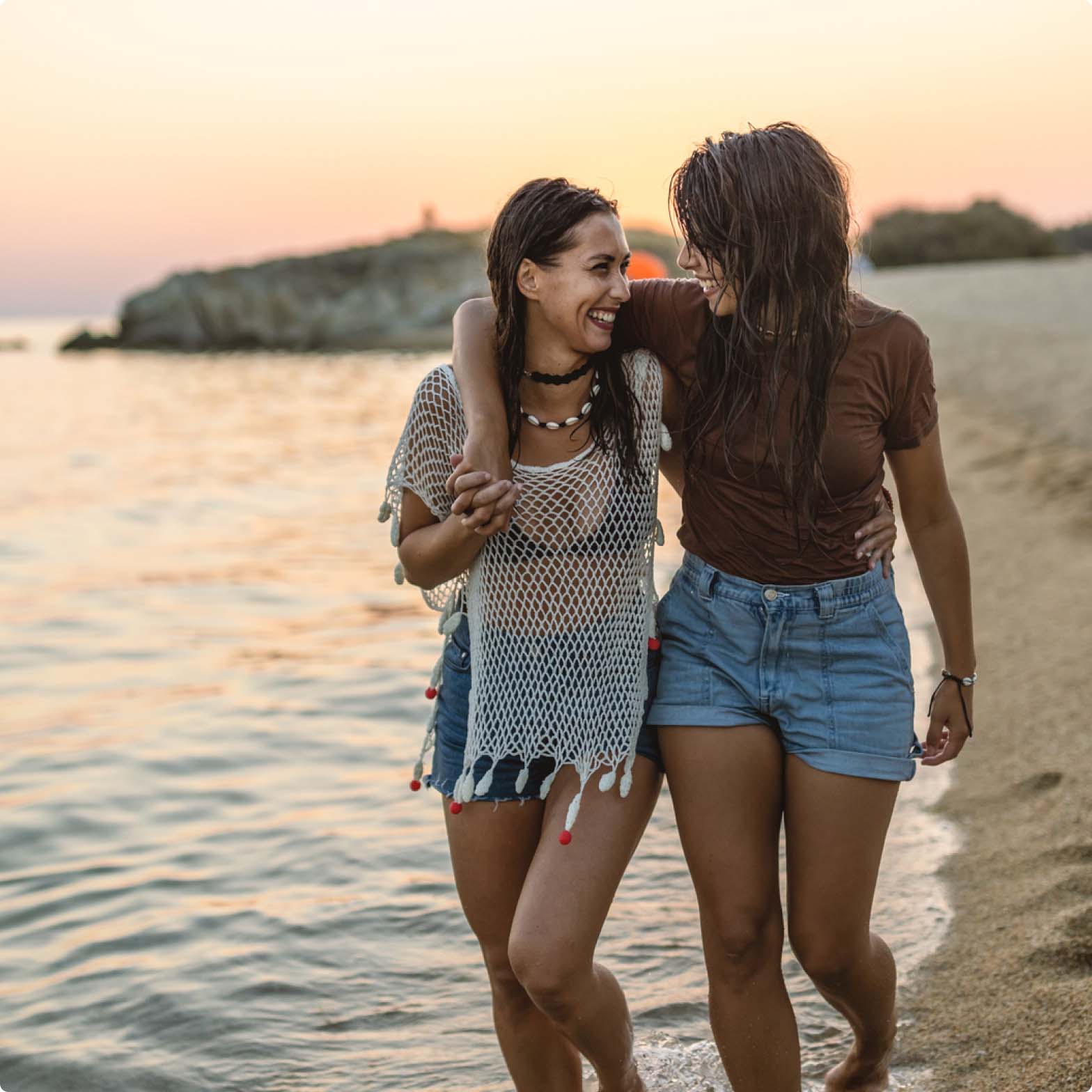 Two women holding each other and smiling while walking along the beach