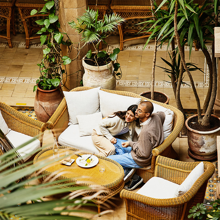 A couple sitting on a sofa in a hotel lobby surrounded by indoor plants