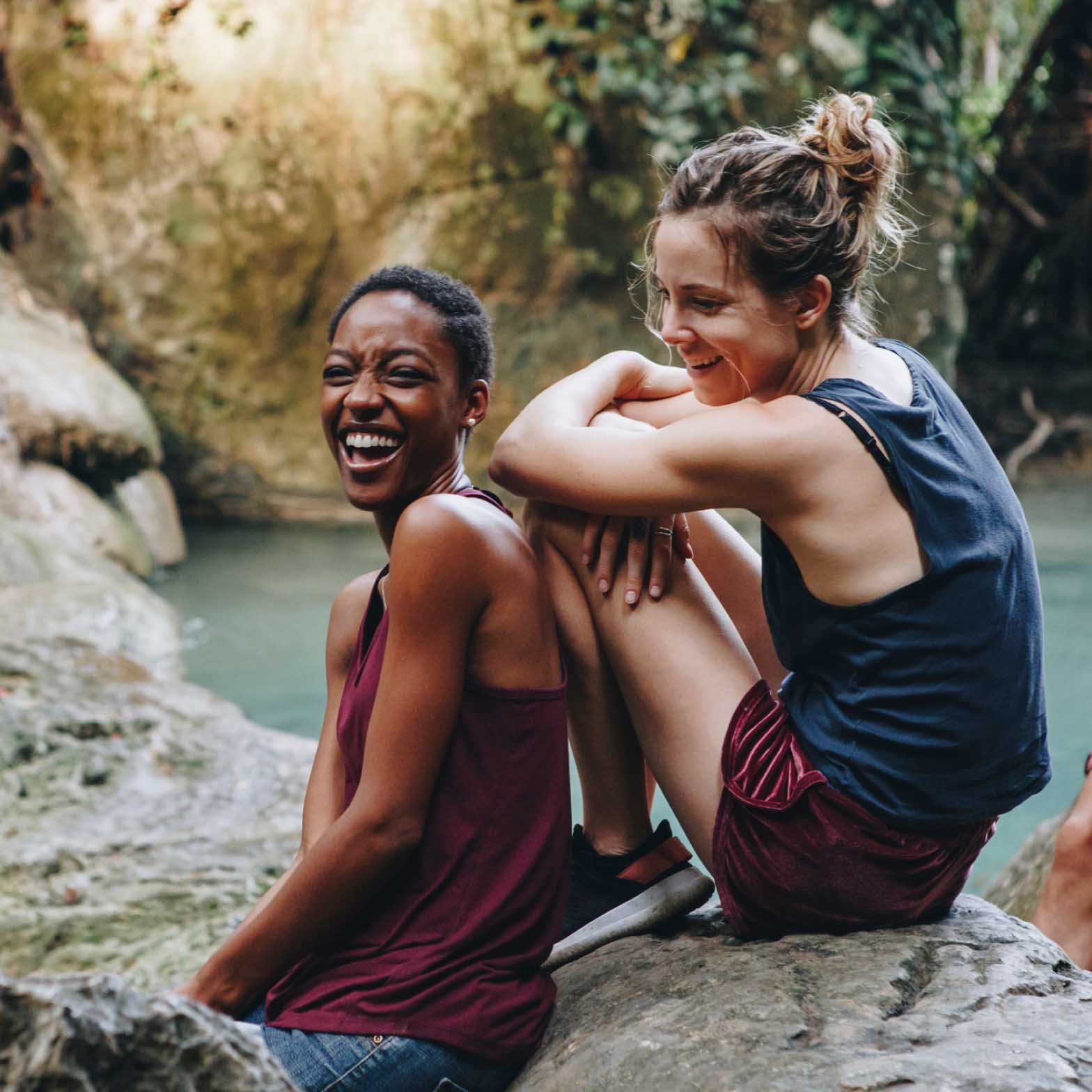 Women laughing sitting on rocks next to a waterfall