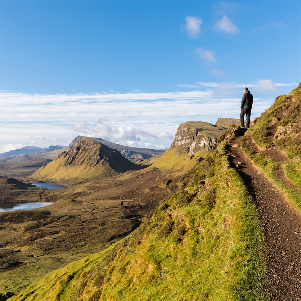 A man standing on a narrow path looking down at the Scottish Highlands