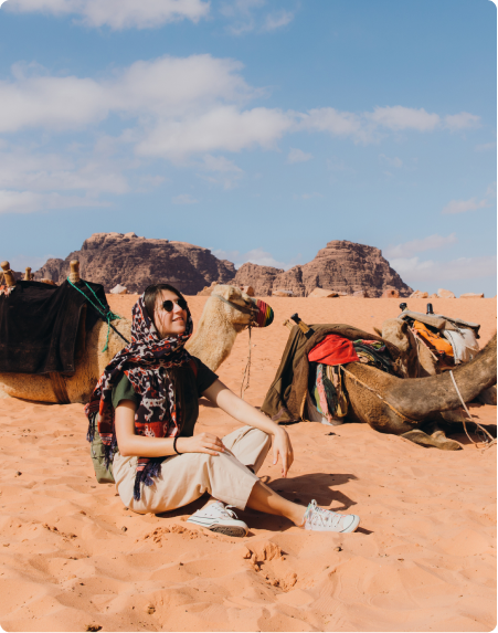 A young woman sits in the desert next to a camel