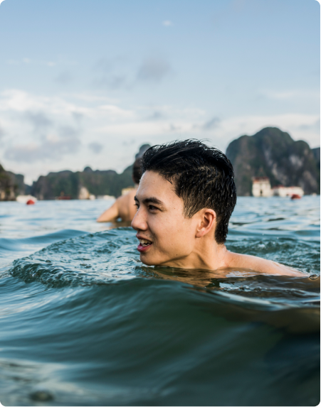 A young man takes a swim in a lake with mountains in the background