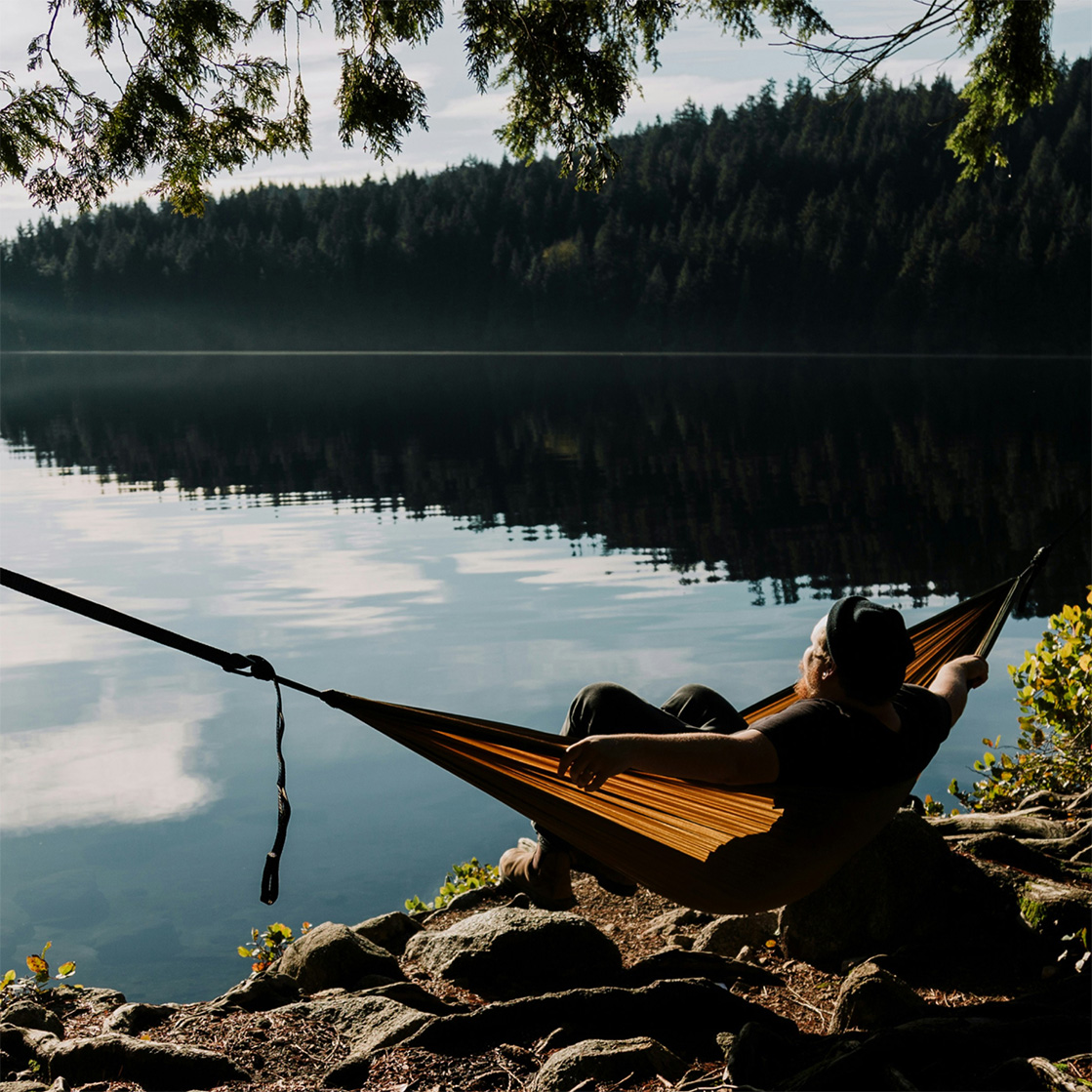 Person relaxing in a hammock by a calm forest lake, surrounded by rocks and trees. Person relaxing in a hammock by a calm forest lake, surrounded by rocks and trees.